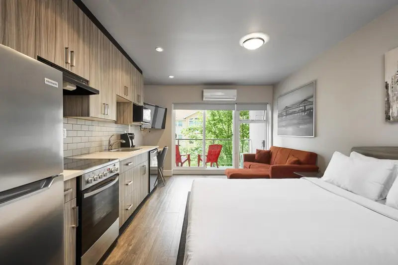 Une kitchenette moderne s'ouvre sur un espace de vie avec un canapé et un lit.