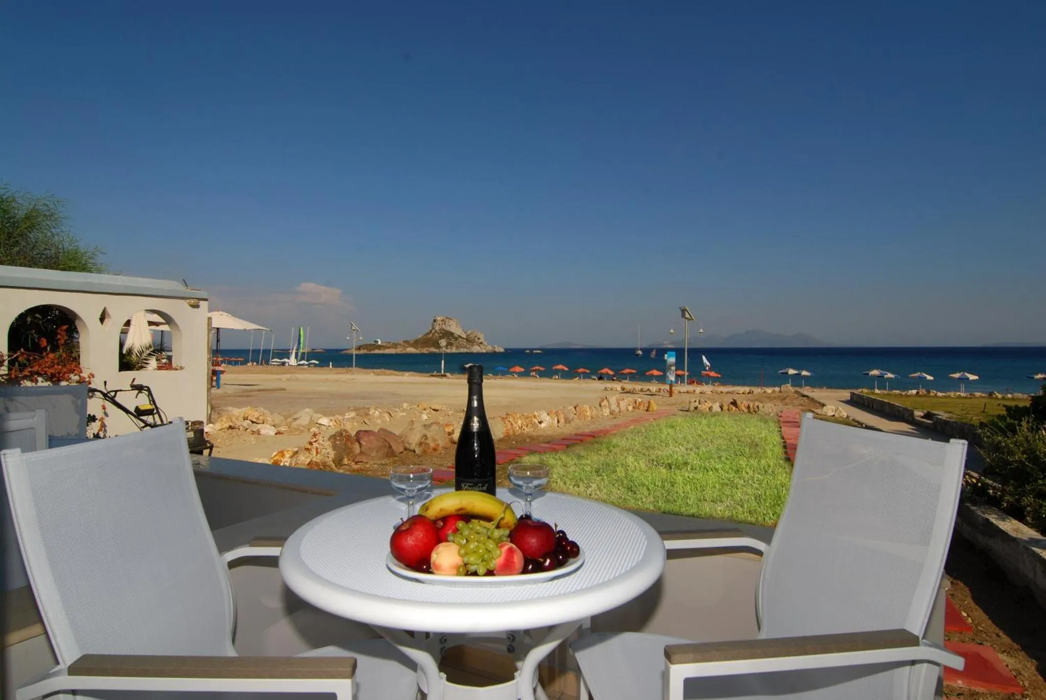 Table ronde avec fruits et boissons sur une terrasse ensoleillée face à la mer.