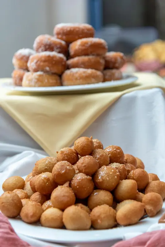 Une pyramide de beignets recouverts de sucre est présentée sur une table recouverte d'une nappe jaune.