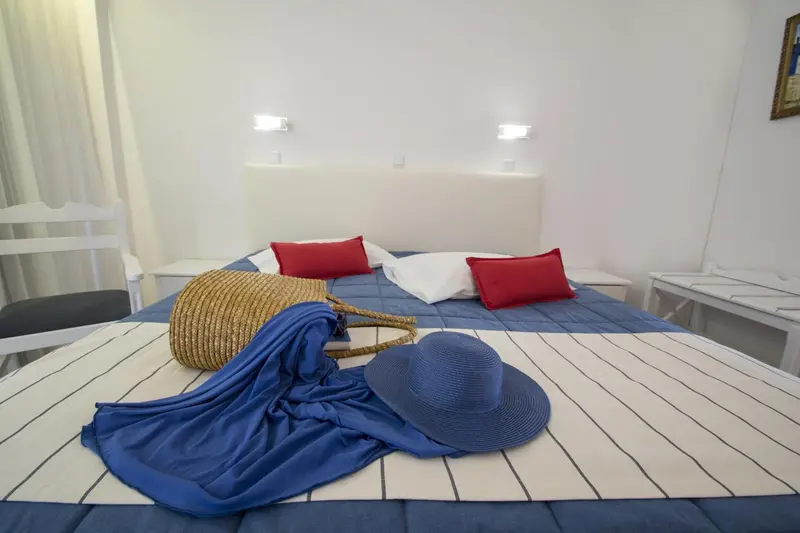 Une chambre lumineuse avec un lit recouvert d'une courtepointe rayée et de coussins rouges.