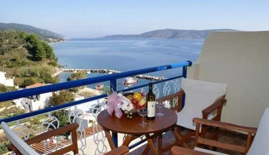 Une table ronde avec des fruits et des boissons est mise en scène sur une terrasse avec vue sur la mer.