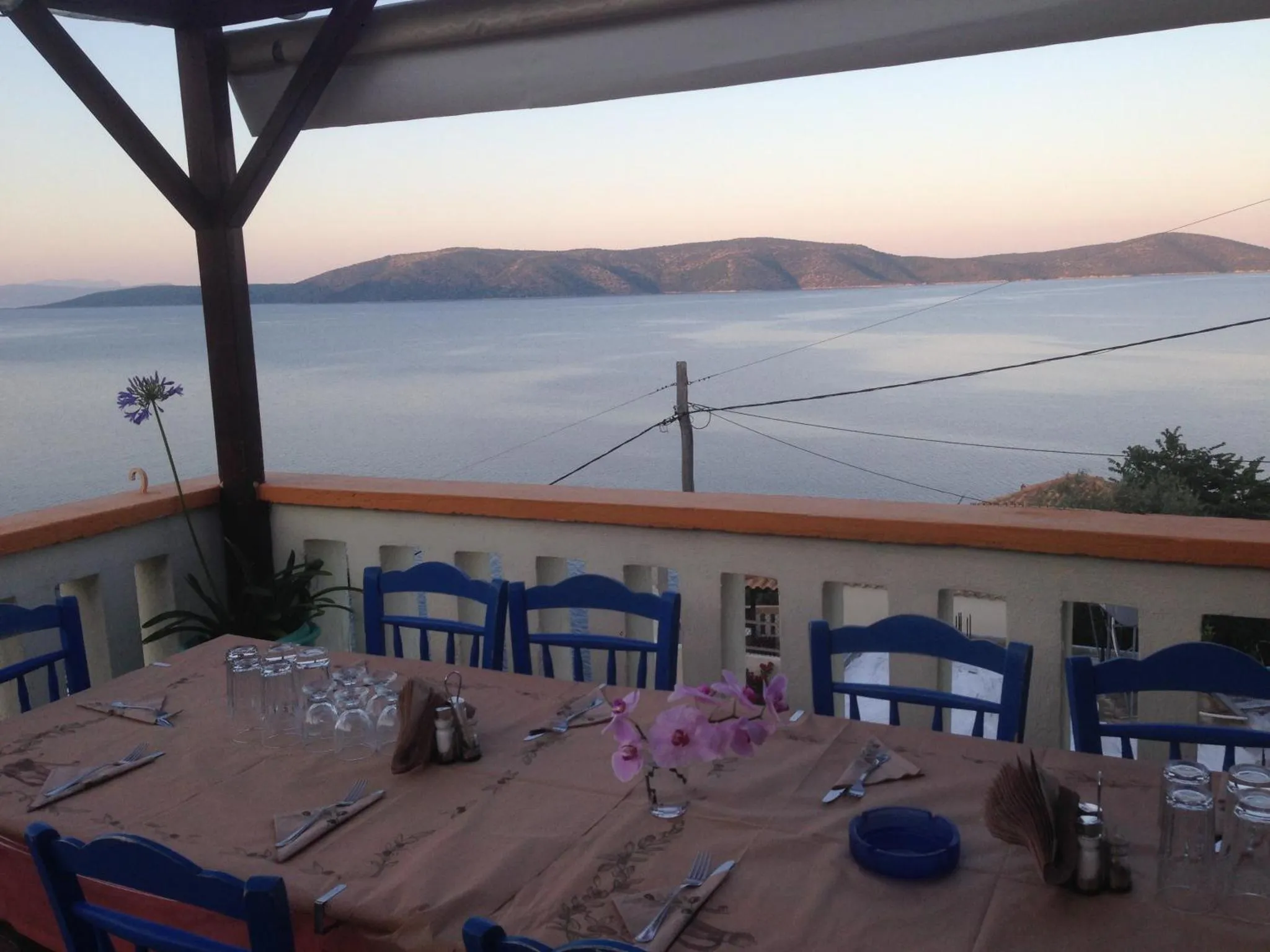 Une table dressée sur une terrasse surplombe la mer au coucher du soleil.