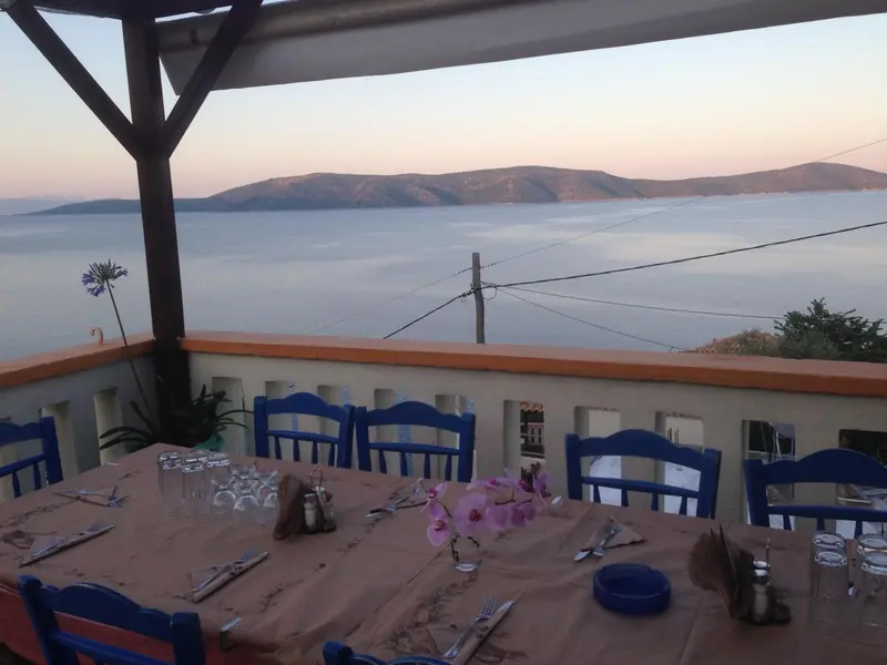 Une table dressée sur une terrasse surplombe la mer au coucher du soleil.