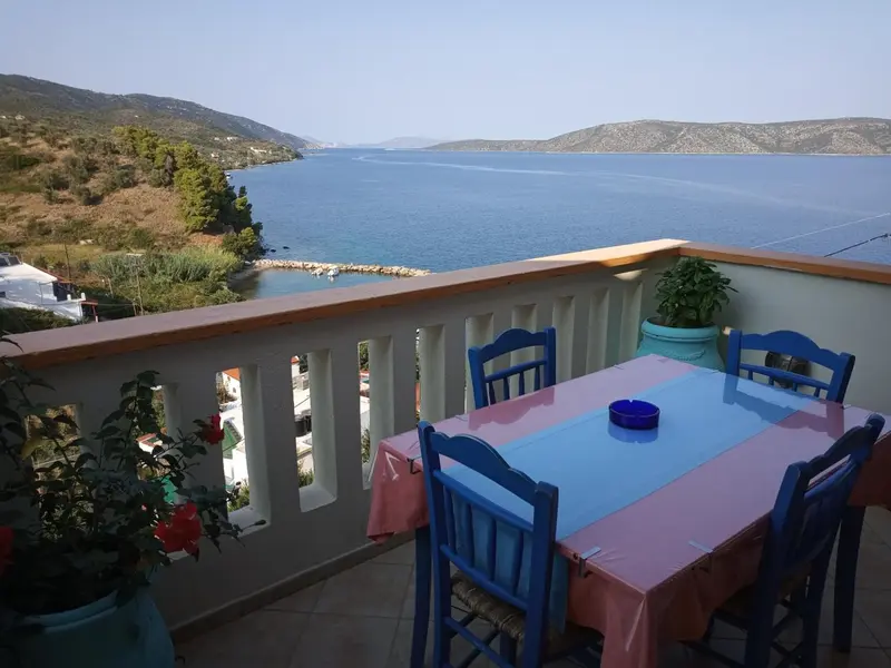 Table et chaises bleues sur une terrasse ensoleillée avec vue sur la mer.