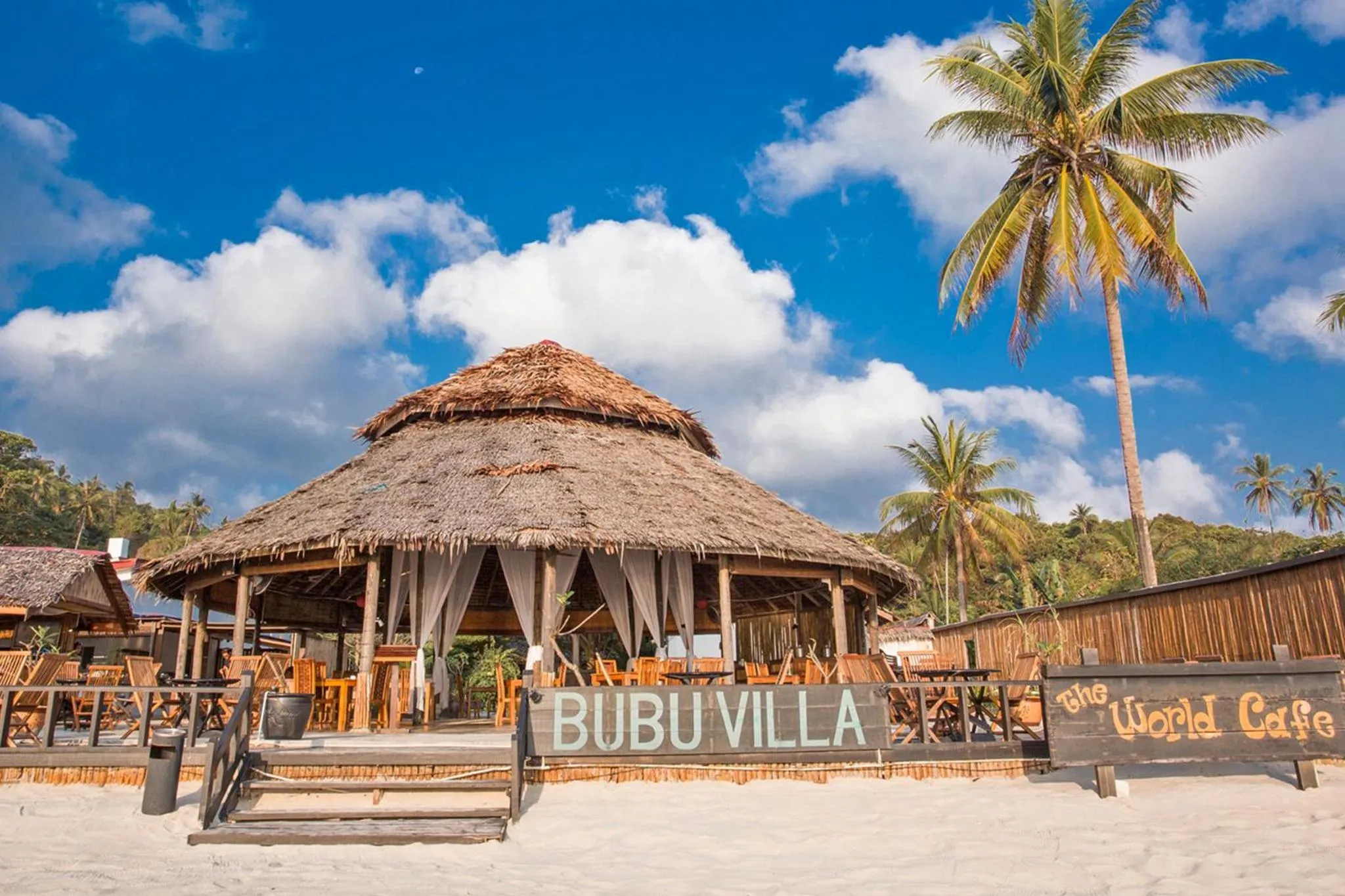 Un restaurant de plage avec une toiture en chaume et des tables en bois.
