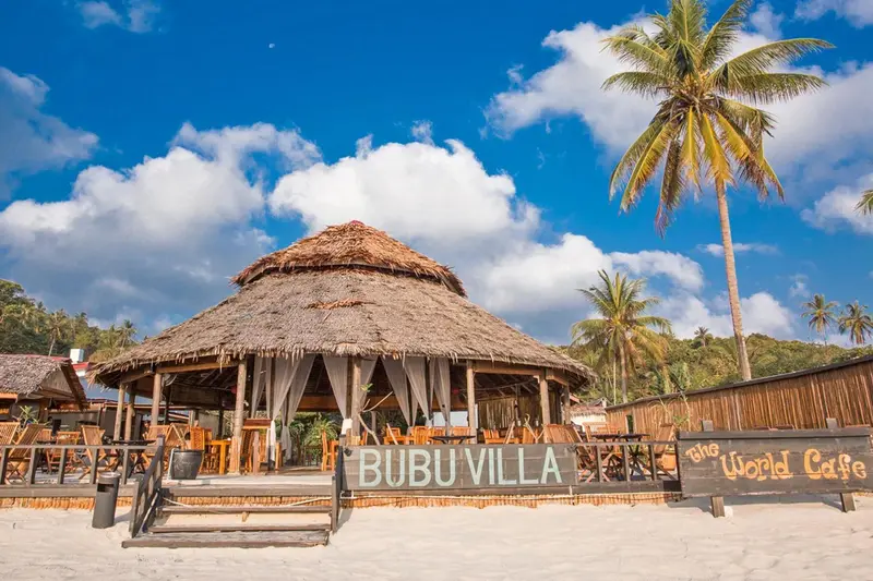 Un restaurant de plage avec une toiture en chaume et des tables en bois.
