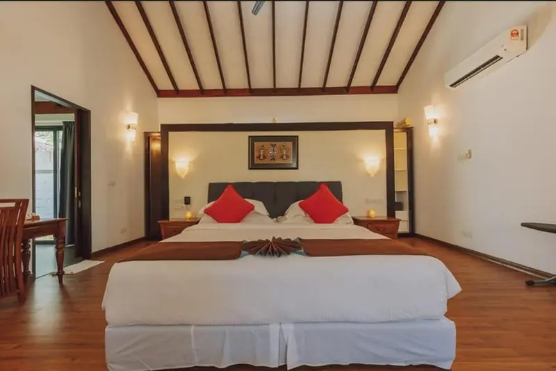 Une chambre lumineuse avec un grand lit recouvert d'une courtepointe blanche et de coussins rouges.