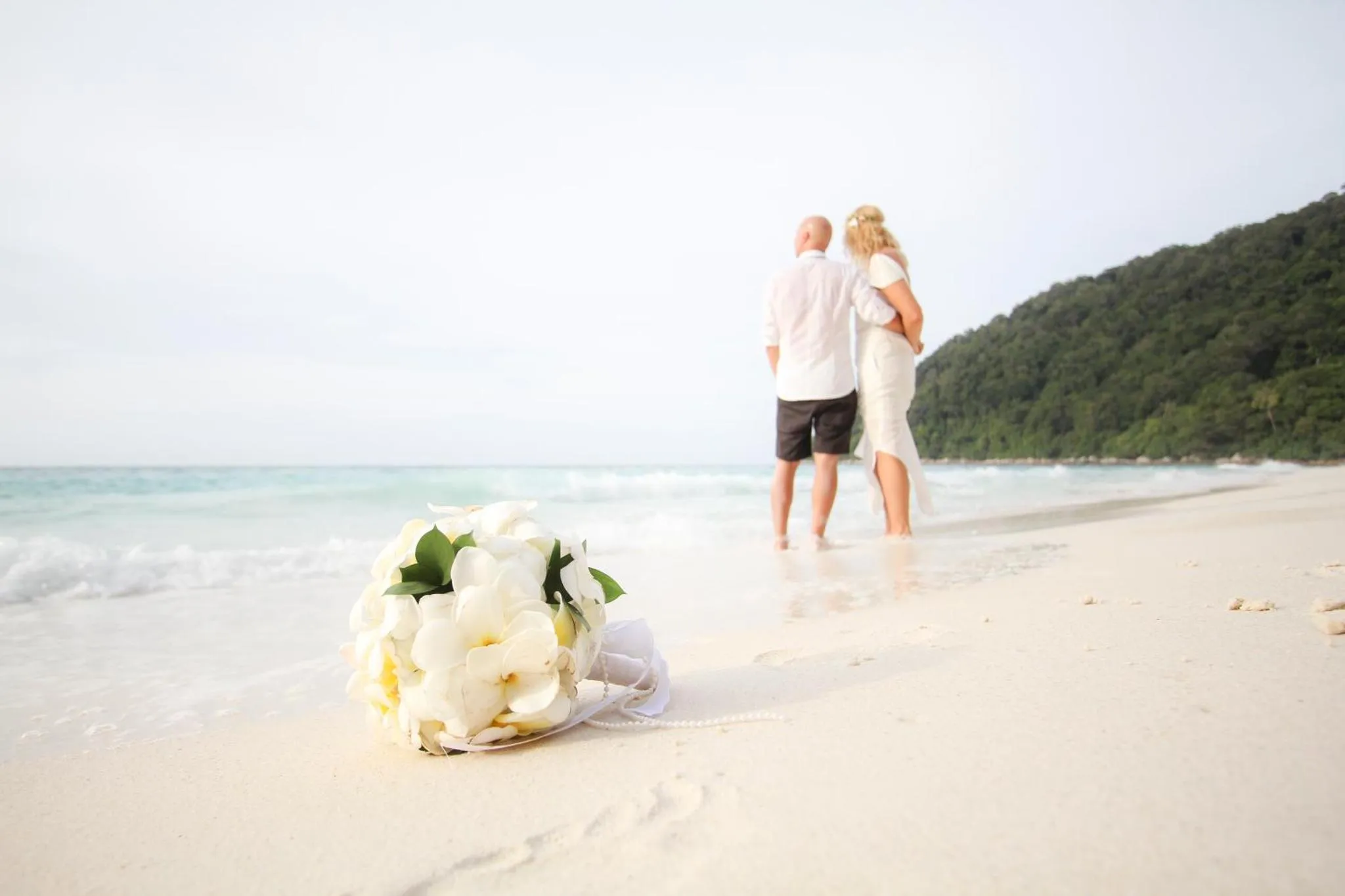 Un couple se tient sur une plage de sable blanc face à la mer.
