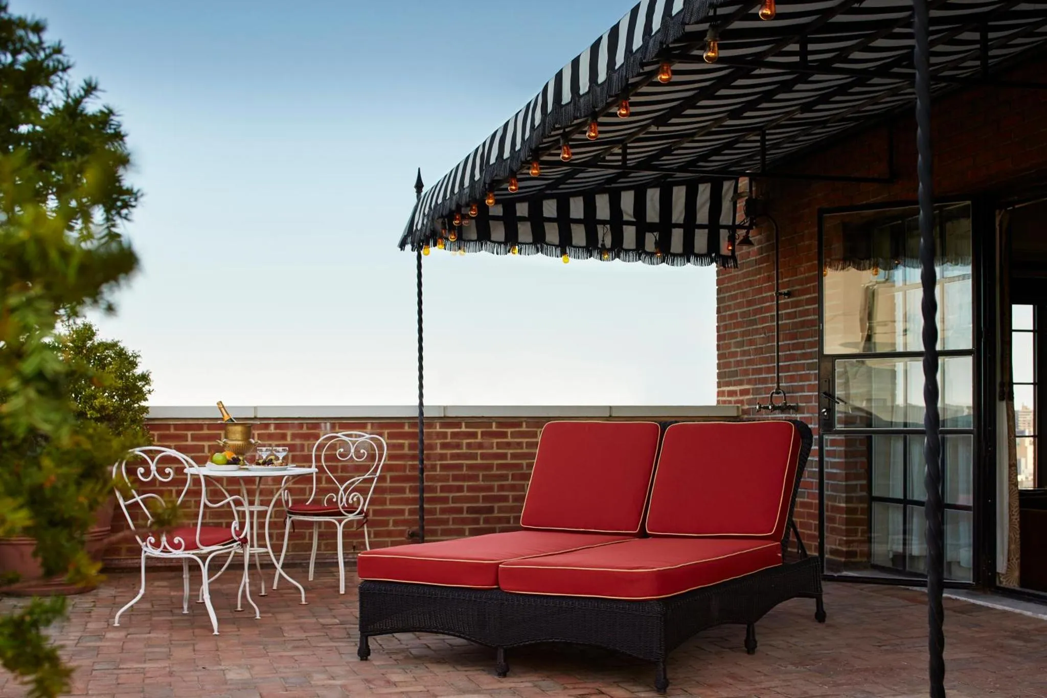 Terrasse ombragée avec mobilier de jardin rouge et blanc.