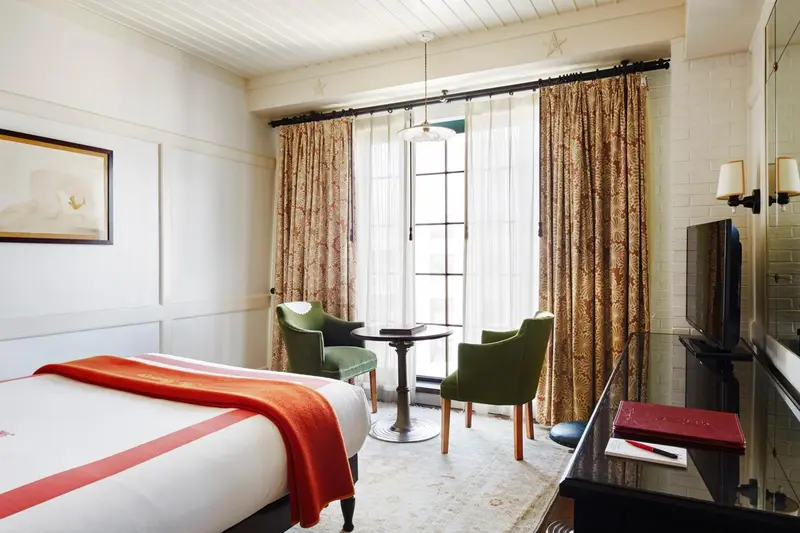 Une chambre lumineuse avec un lit et deux fauteuils près d'une porte-fenêtre.