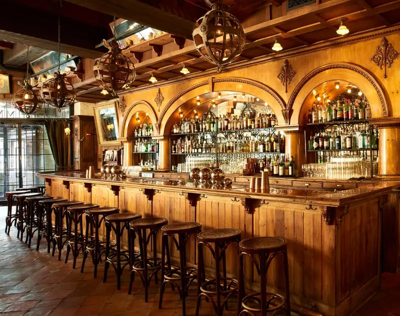 Un long comptoir en bois est aligné de tabourets hauts dans une salle décorée de luminaires et d'arches.