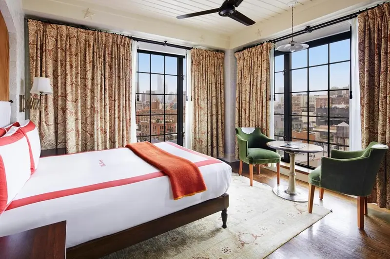 Une chambre lumineuse avec un lit et un coin salon près des fenêtres.