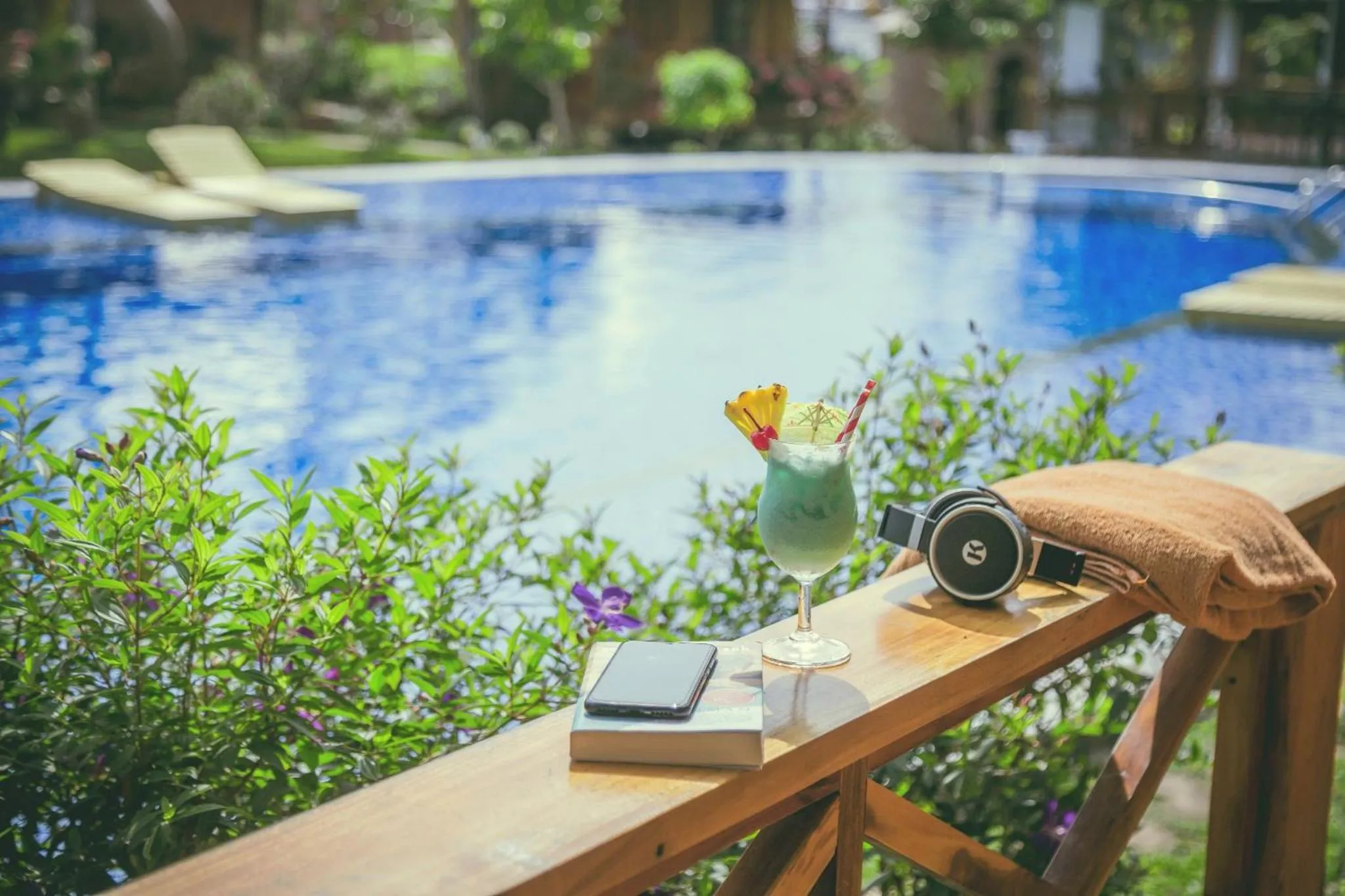 Un cocktail rafraîchissant et un téléphone reposent sur une rambarde en bois au bord d'une piscine.