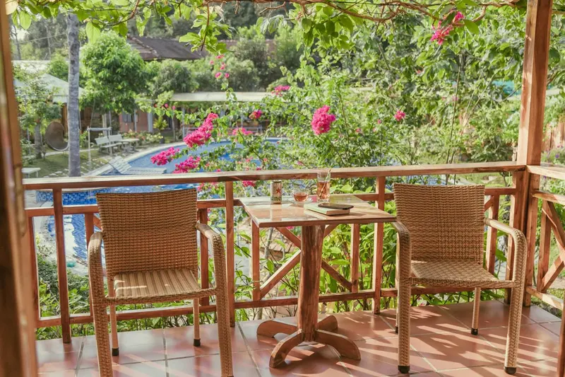 Terrasse avec table et chaises en osier, vue sur une piscine et une végétation luxuriante.