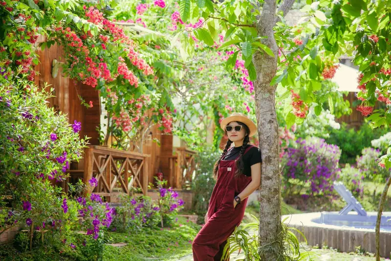 Une jeune femme adossée à un arbre en fleurs devant des bâtiments.