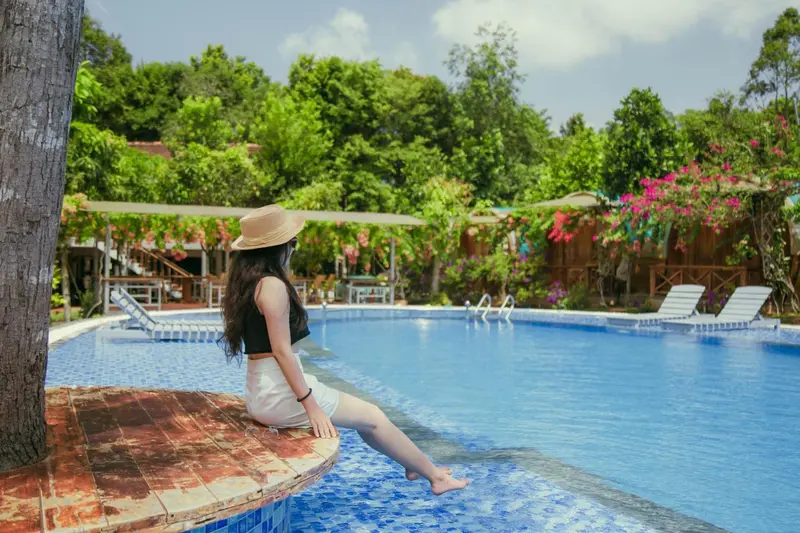 Une femme assise au bord d'une piscine ensoleillée, entourée de végétation luxuriante.