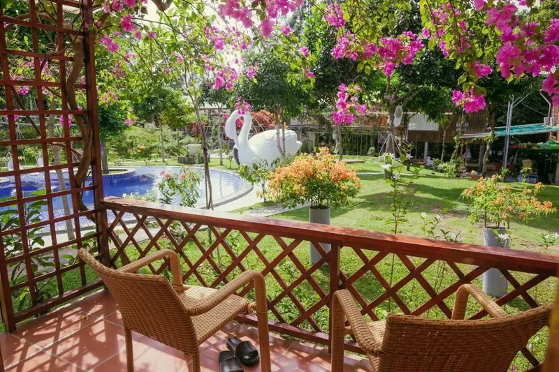 Deux fauteuils en osier sur une terrasse en bois donnant sur un jardin fleuri et une piscine.