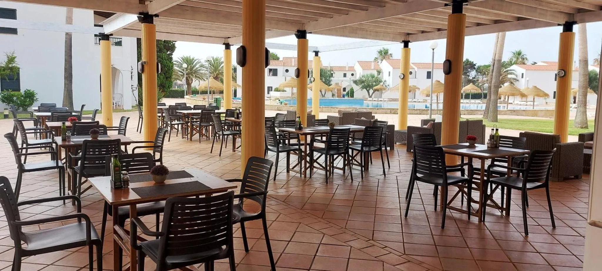 Terrasse ombragée avec tables et chaises pour les repas.