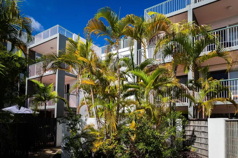 Façade d'un bâtiment blanc avec des balcons et une végétation tropicale.