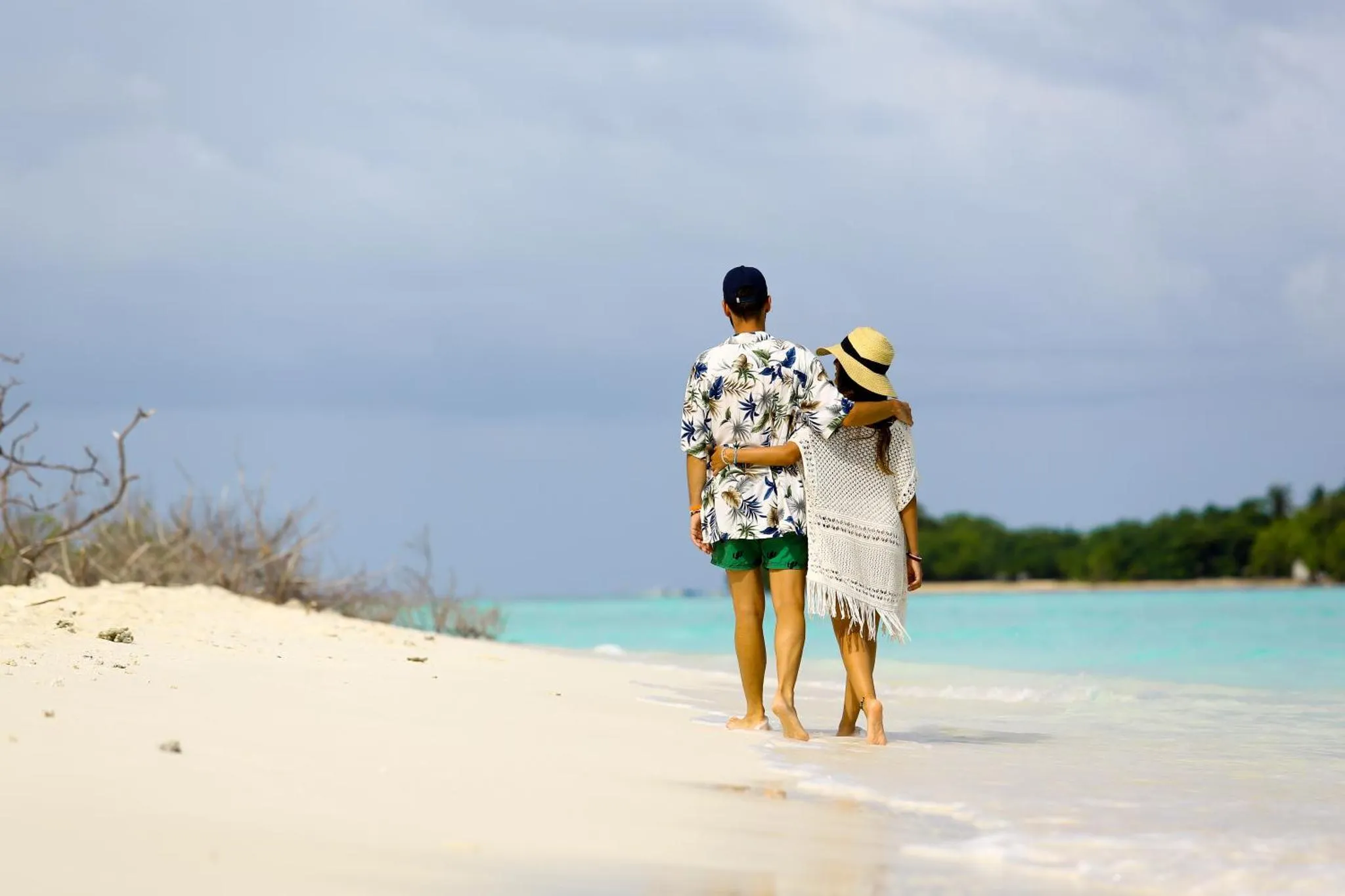 Un couple marche sur une plage de sable blanc face à la mer turquoise.
