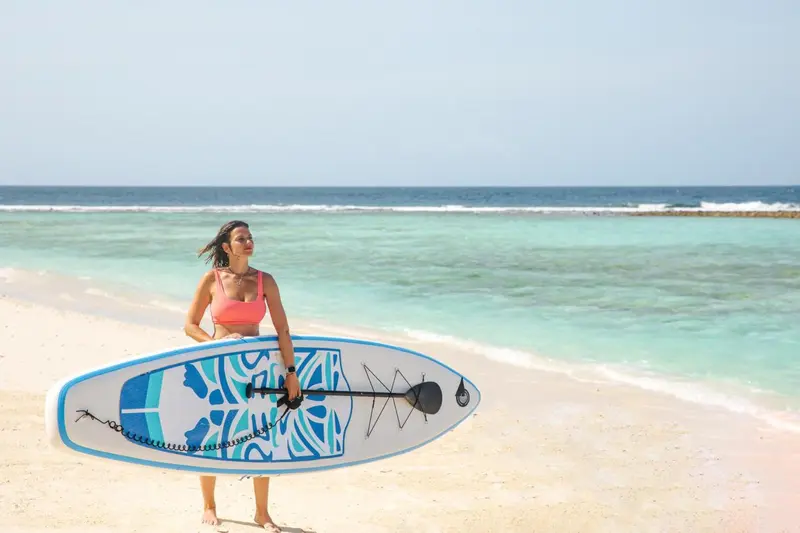 Une femme se tient sur une plage de sable blanc avec une planche de paddle.