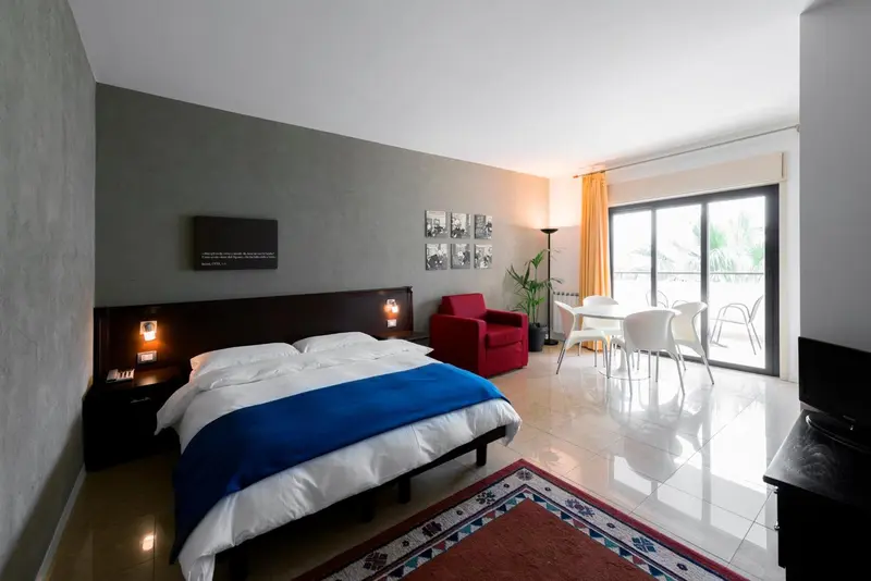 Une chambre lumineuse avec un lit fait et un coin repas près d'une baie vitrée.