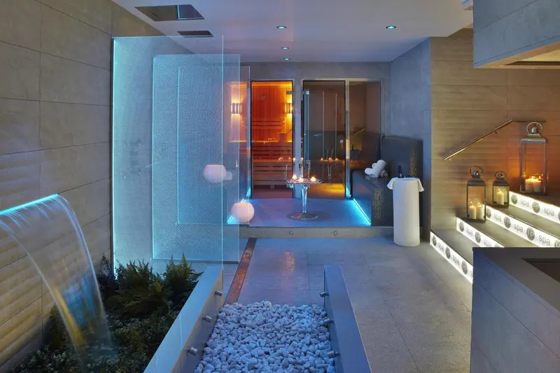 Espace de relaxation avec cascade lumineuse et accès à un sauna.