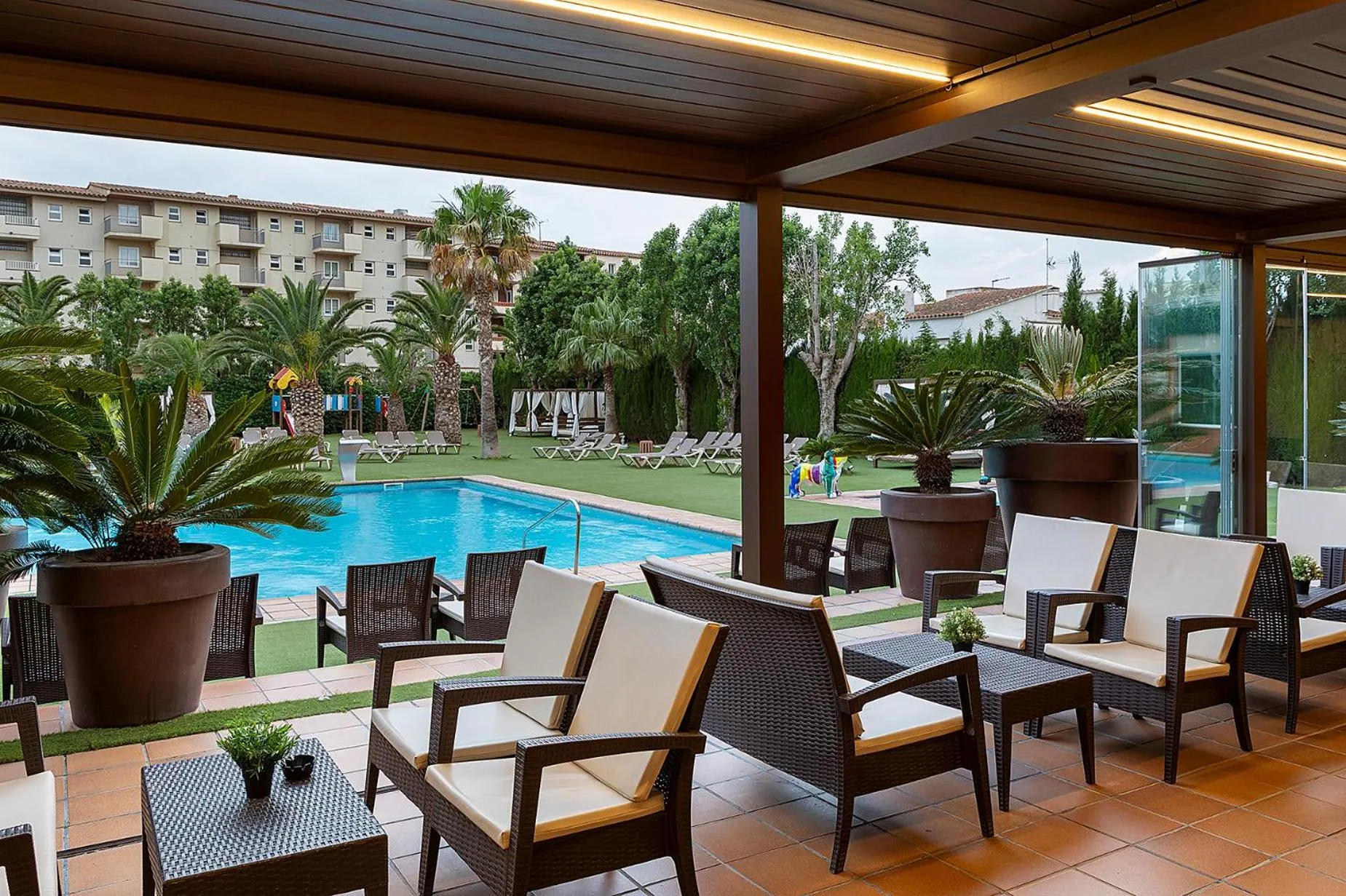 Espace de détente extérieur avec mobilier et vue sur une piscine et des palmiers.