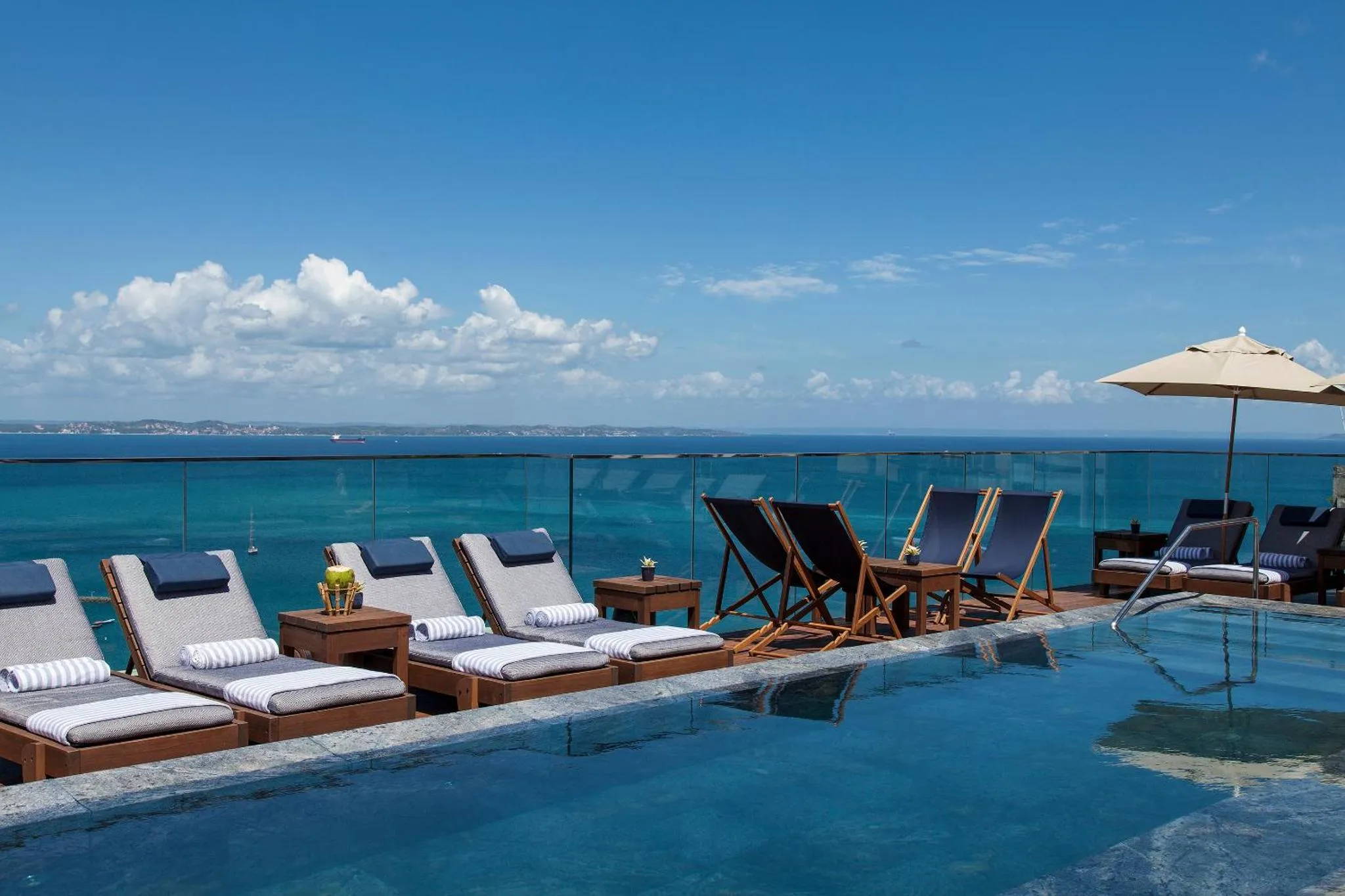 Transats et tables basses au bord d'une piscine à débordement avec vue sur la mer.