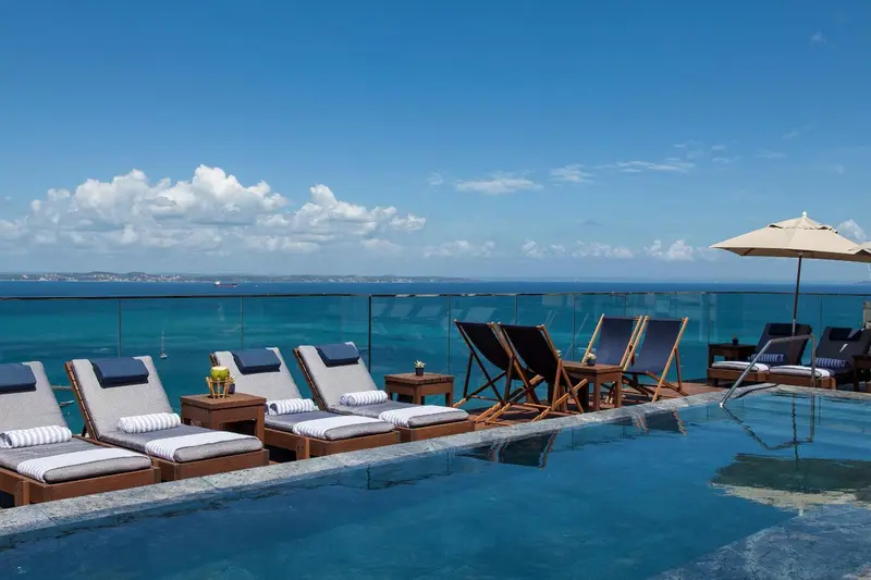 Transats et tables basses au bord d'une piscine à débordement avec vue sur la mer.