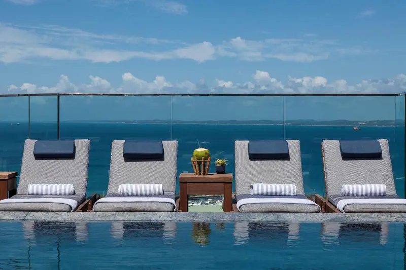 Transats et petite table d'appoint au bord d'une piscine à débordement avec vue sur la mer.
