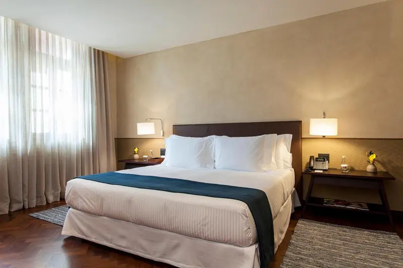 Une chambre d'hôtel lumineuse avec un grand lit recouvert d'une courtepointe blanche et bleue.