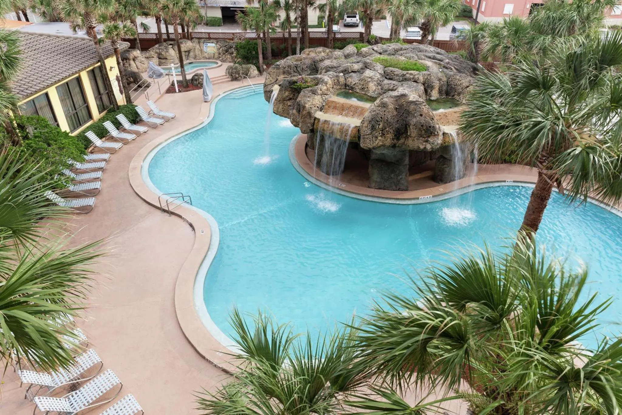 Piscine sinueuse avec cascades et rochers, entourée de transats et de végétation tropicale.