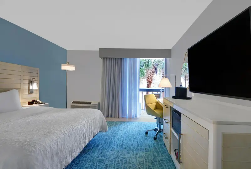Une chambre lumineuse avec un grand lit et un bureau près d'une fenêtre.