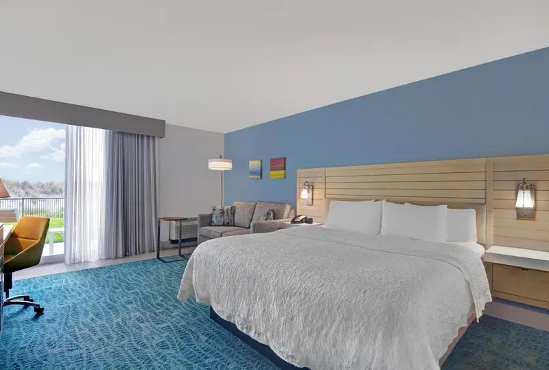 Une chambre lumineuse avec un grand lit et un coin salon donnant sur une vue extérieure.