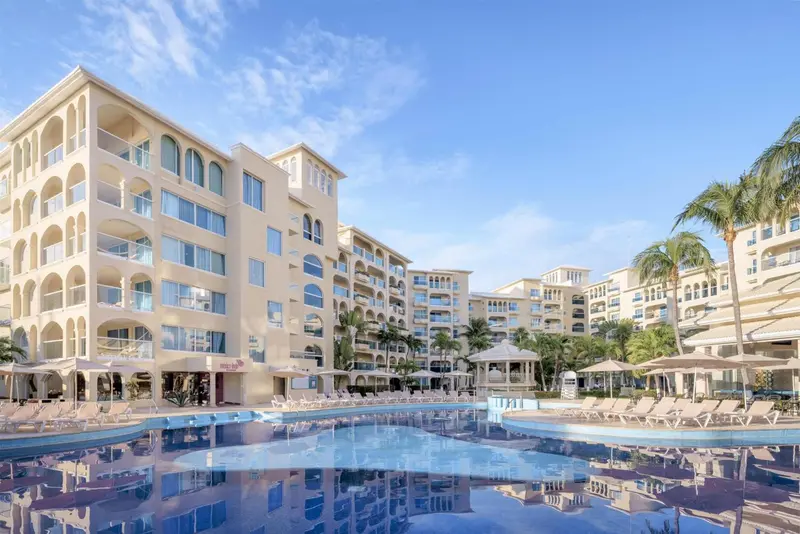 Vue d'un complexe hôtelier avec piscine et palmiers sous un ciel bleu.