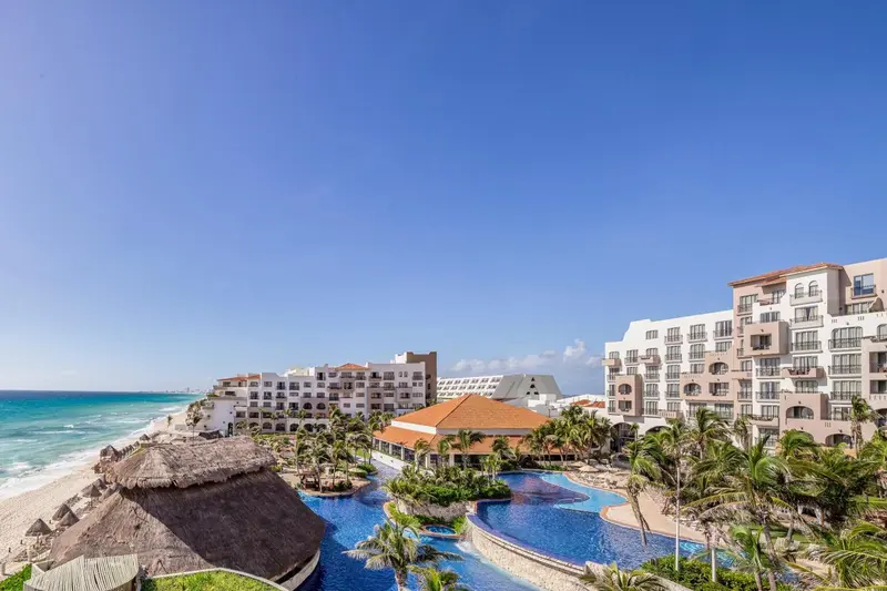 Vue aérienne d'un complexe hôtelier blanc avec piscine et végétation tropicale face à la mer.