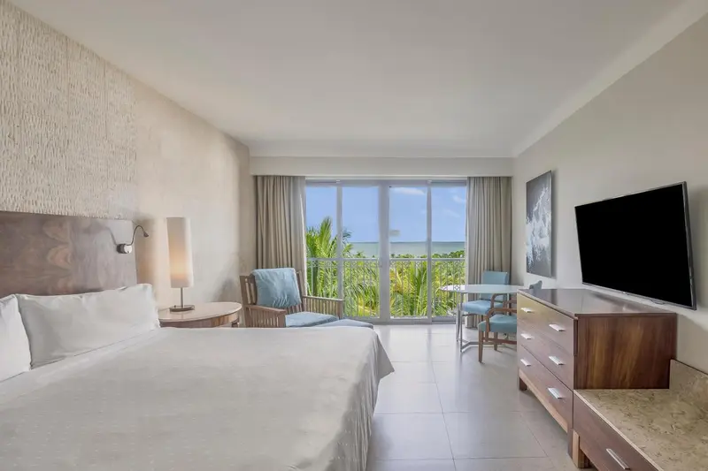 Chambre lumineuse avec un lit double et une vue sur la végétation tropicale.