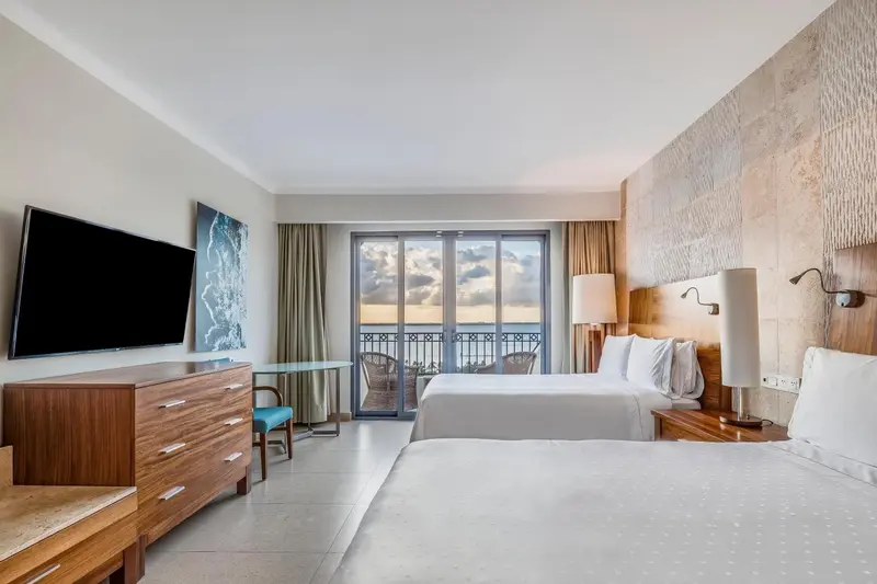 Chambre lumineuse avec deux lits et balcon donnant sur la mer.