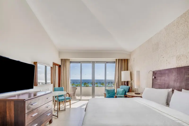 Une chambre lumineuse avec un grand lit et un balcon donnant sur la mer.