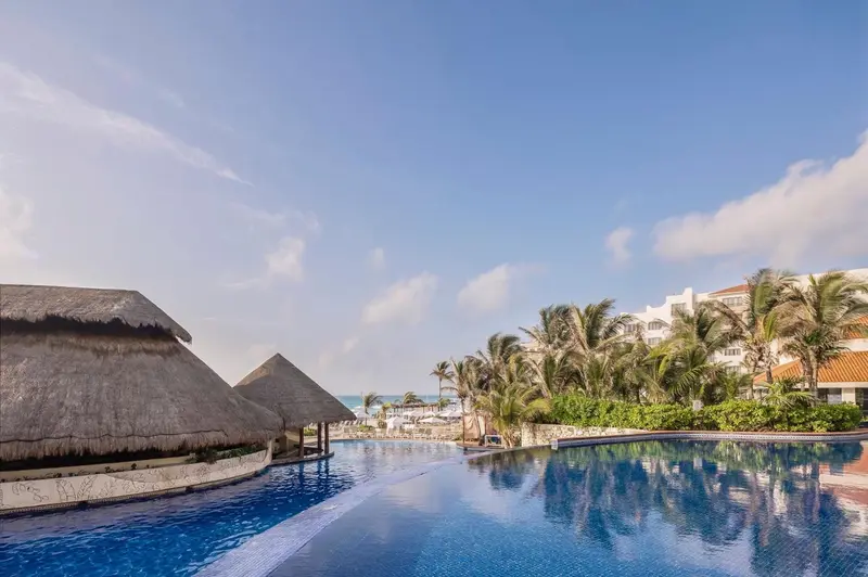 Une piscine bleue reflète le ciel et la végétation tropicale.