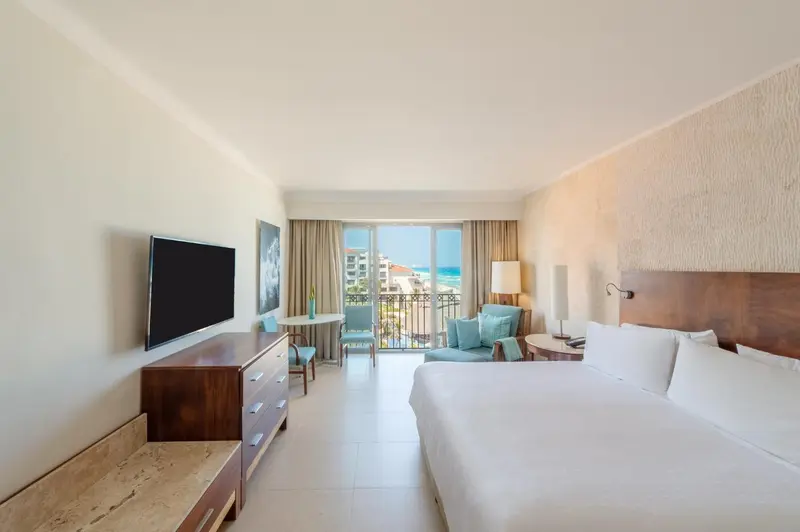 Chambre lumineuse avec un lit blanc et un balcon donnant sur la mer.