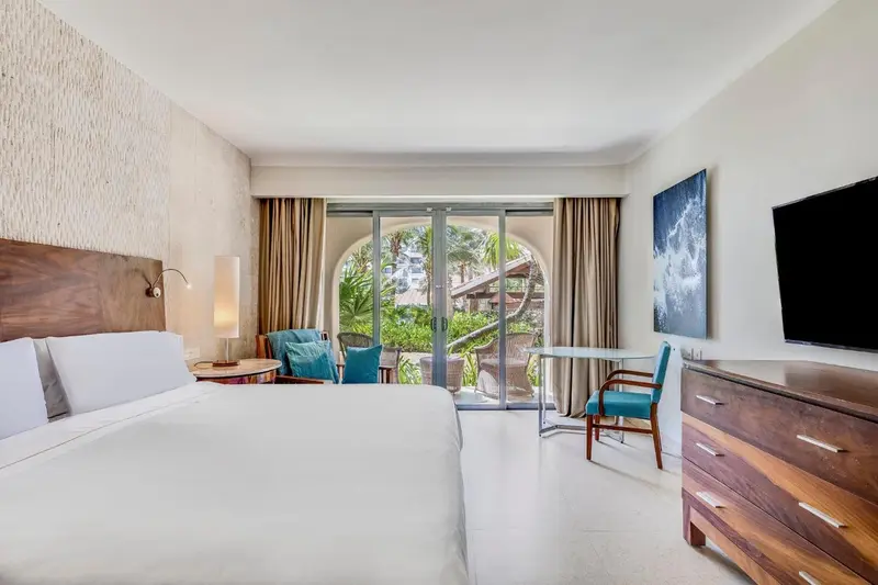 Une chambre lumineuse avec un grand lit et un bureau près d'une baie vitrée.