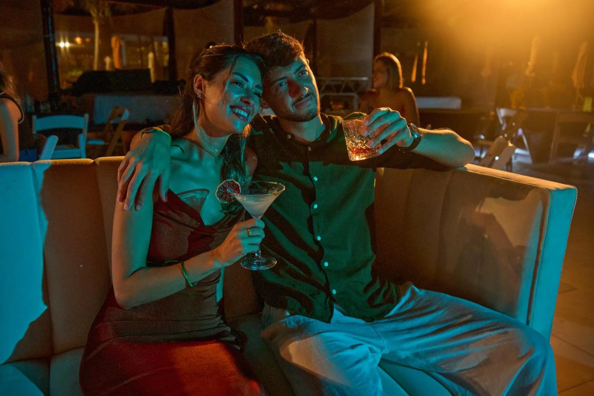 Un couple souriant partage un moment de détente avec des boissons dans un cadre éclairé.