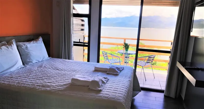 Une chambre lumineuse avec un grand lit donnant sur une terrasse et une vue sur l'eau.