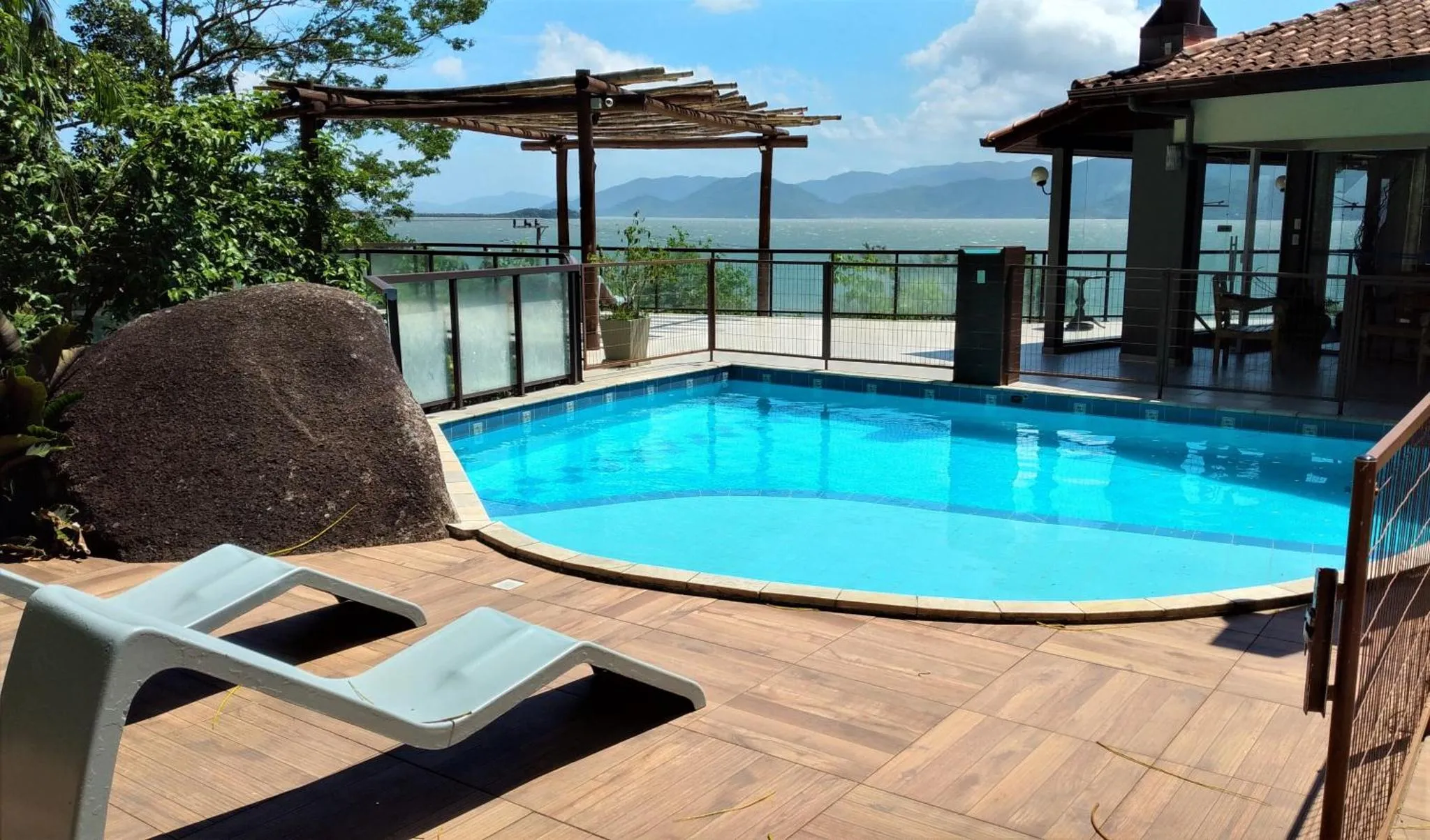 Une piscine turquoise avec des transats sur une terrasse ensoleillée, avec vue sur la mer et les montagnes.