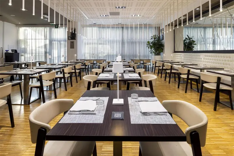 Une salle lumineuse est aménagée avec des tables dressées pour un repas.