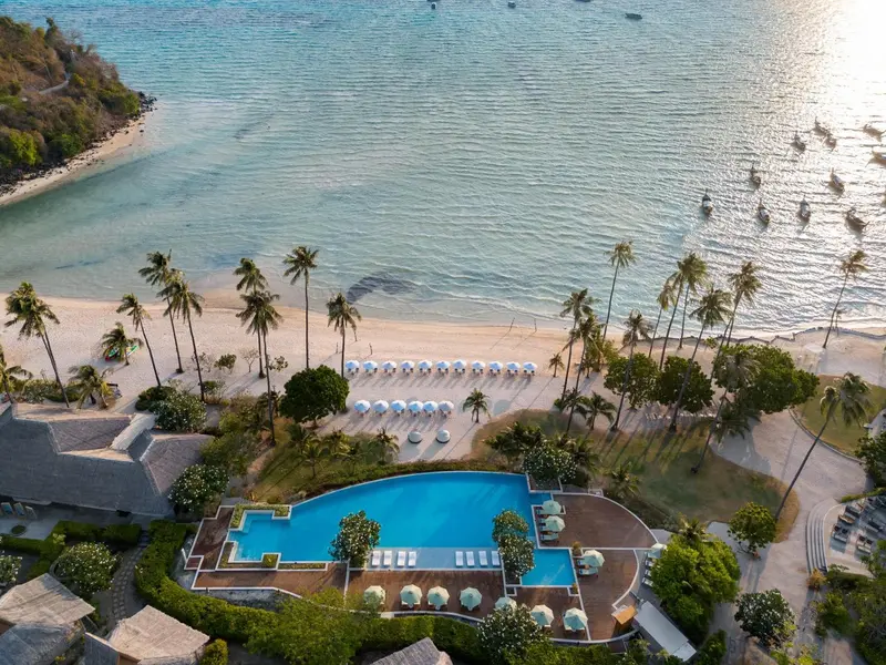 Vue aérienne d'une piscine et d'une plage bordée de palmiers.