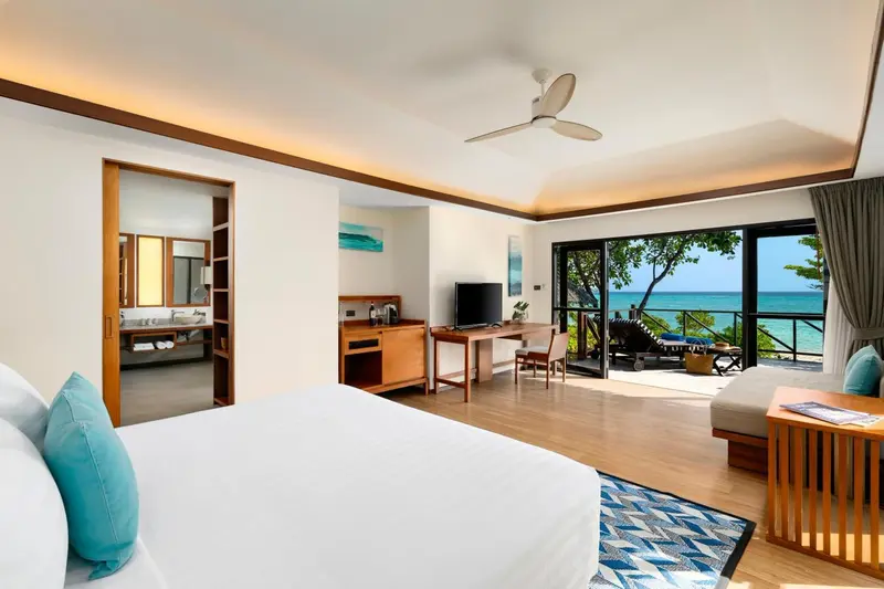 Chambre lumineuse avec un lit blanc et un accès à une terrasse vue sur mer.