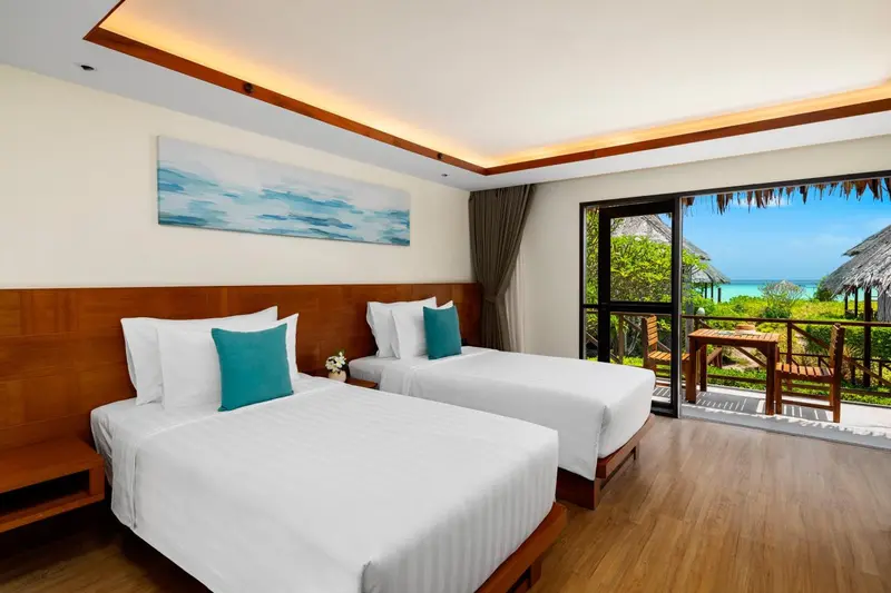 Chambre lumineuse avec deux lits simples donnant sur une vue tropicale.